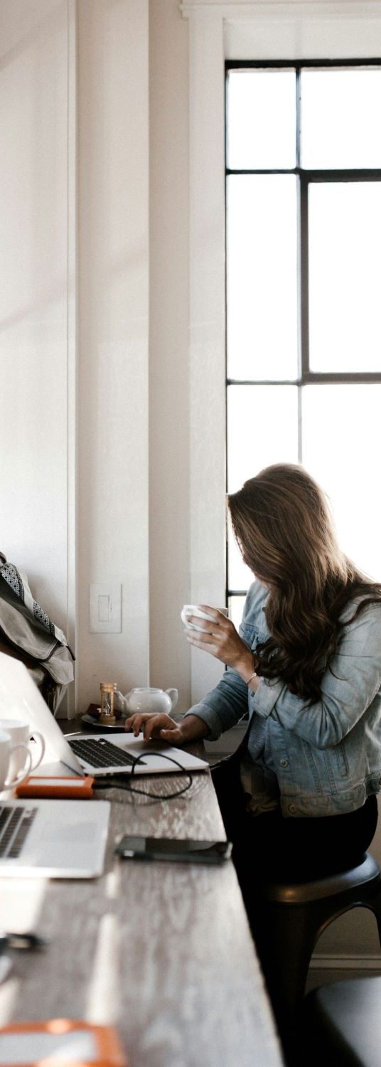 Woman working on a laptop in a bright office with coffee — representing professional English communication and international business.